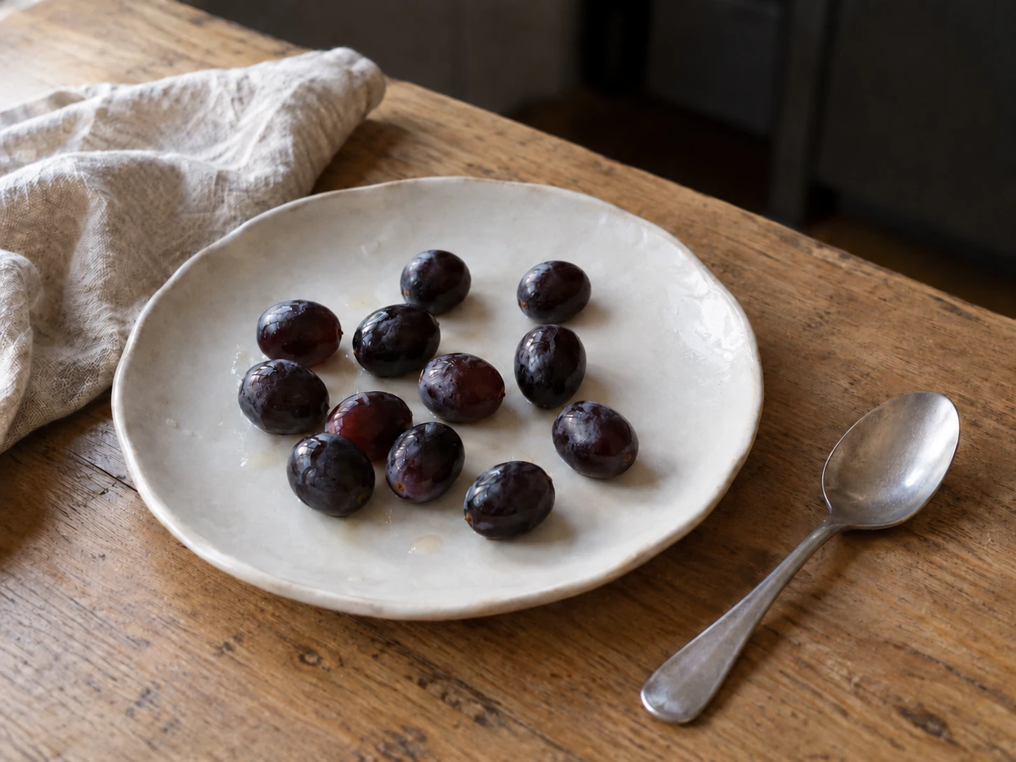 Douze grains de raisin blancs disposés dans une assiette blanche sur un plan de travail en bois clair, éclairés par la lumière naturelle du jour.