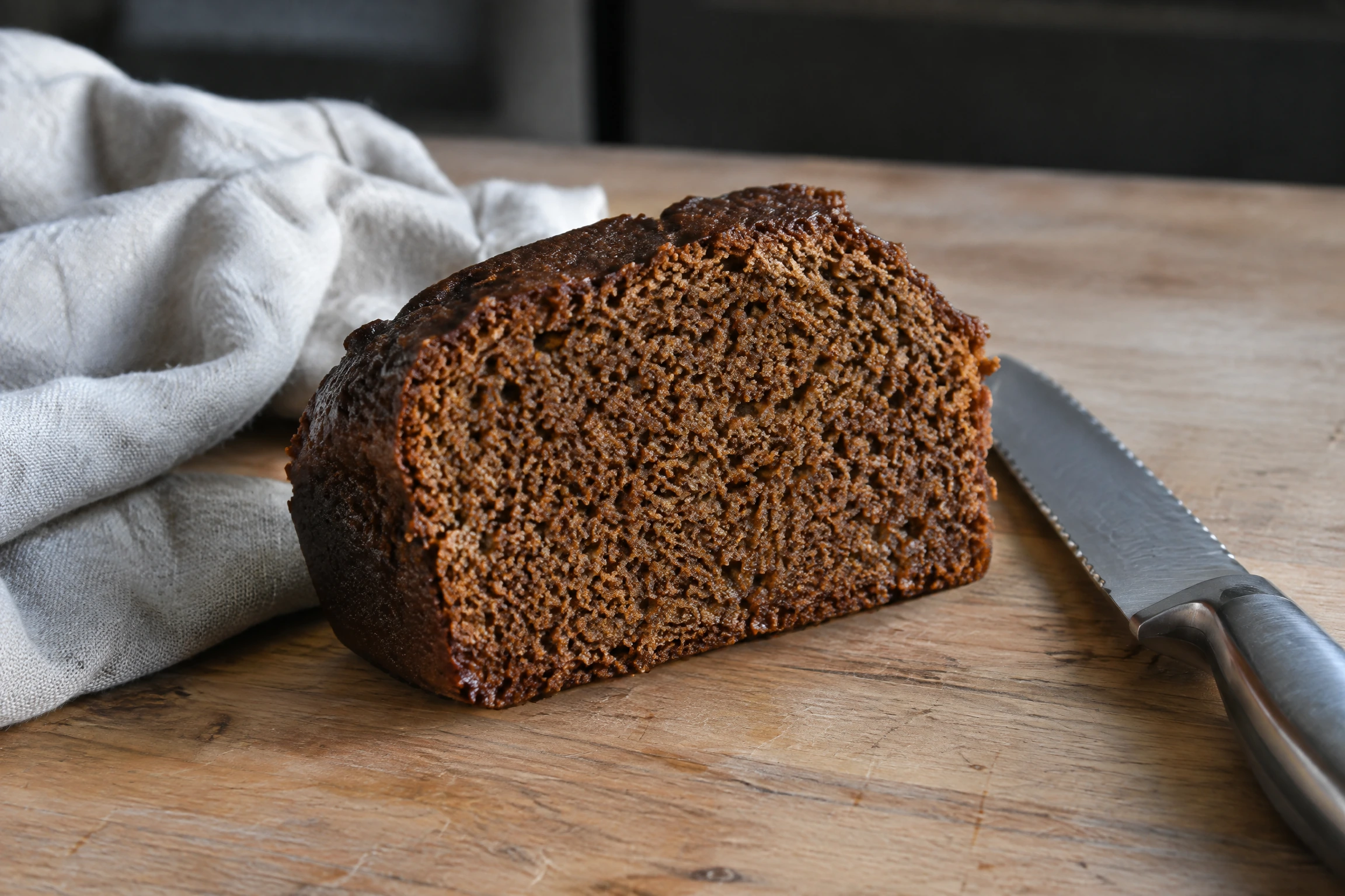 Tranche de pain d'épices fraîchement coupée, présentée sur un plan de travail en bois clair avec un couteau à pain et un torchon en lin.